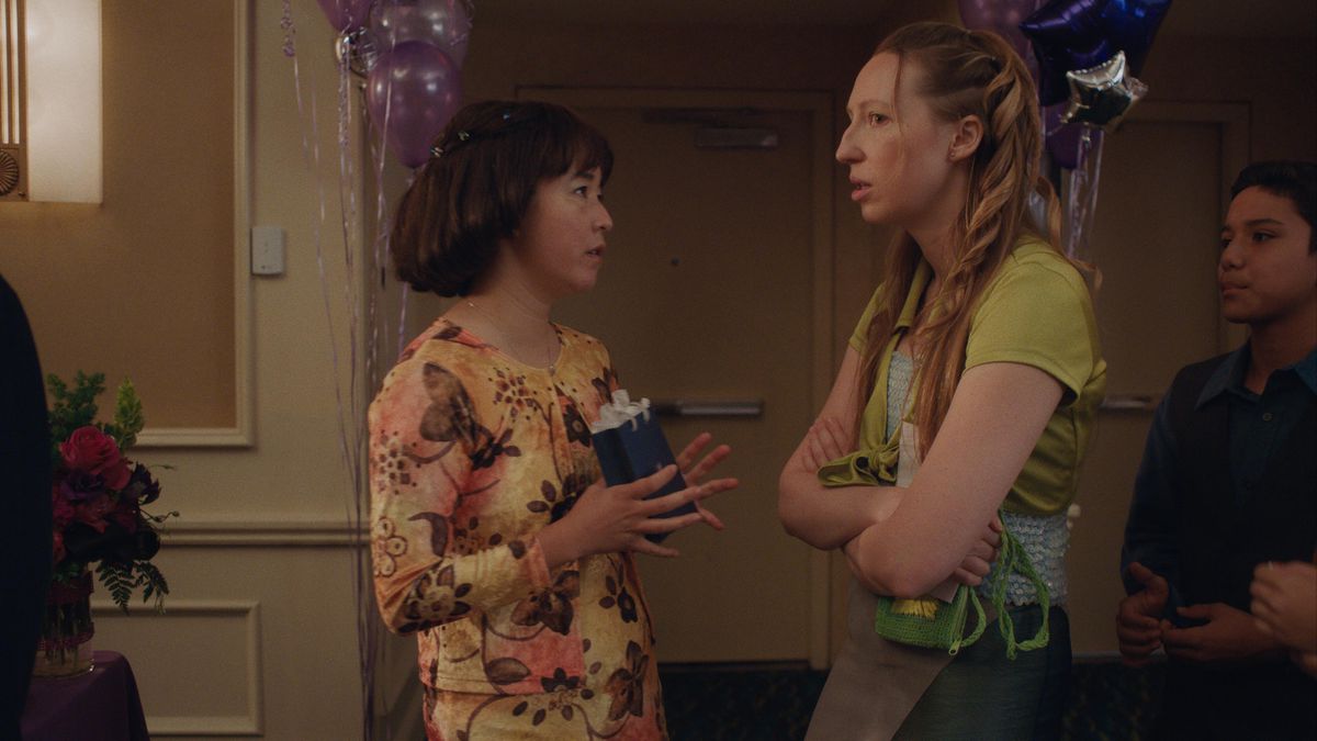 Maya Erskine and Anna Konkle playing tween versions of themselves in Pen15. The two are dressed up for a Bat Mitzvah, and Maya is holding a gift.