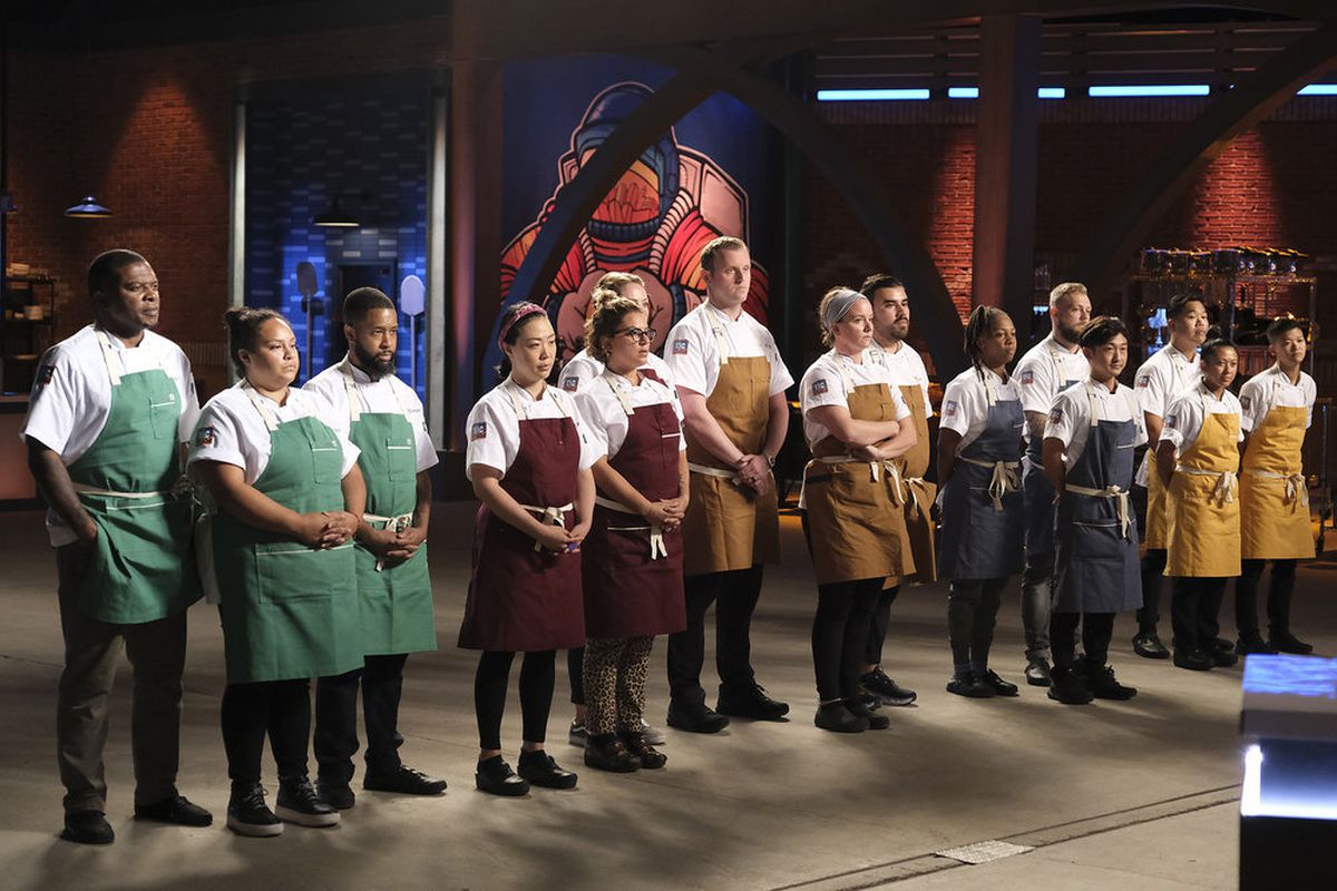 15 ‘Top Chef’ contestants stand awaiting directions from the hosts. 