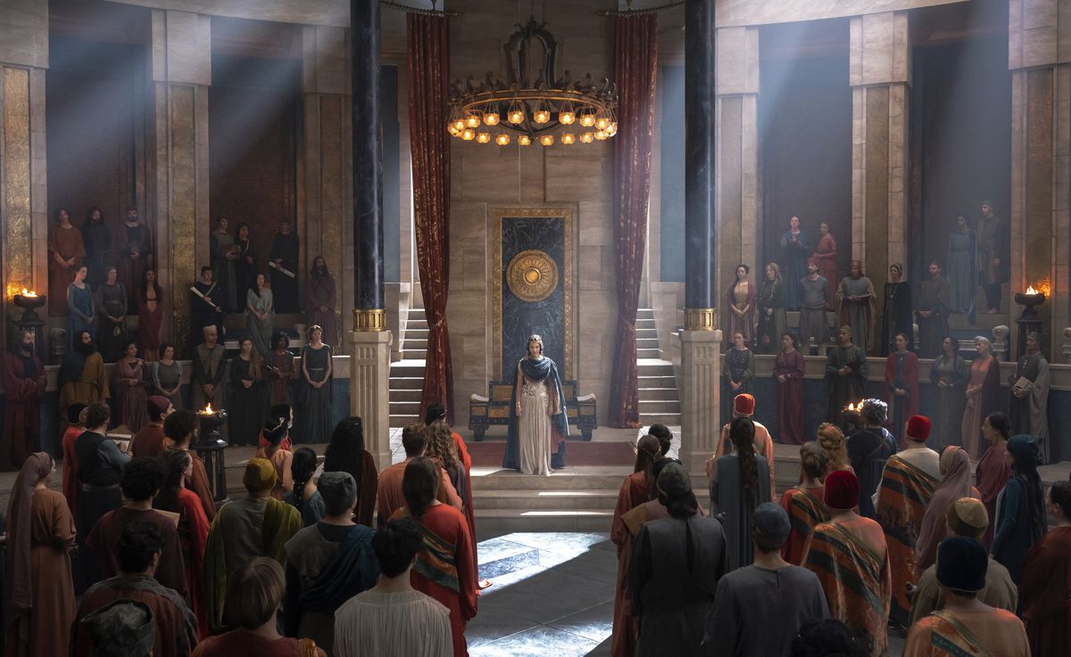 The queen regent of Numenor standing in front of people in the throne room; there are people standing in rows facing her, as well as flanking her on the deis