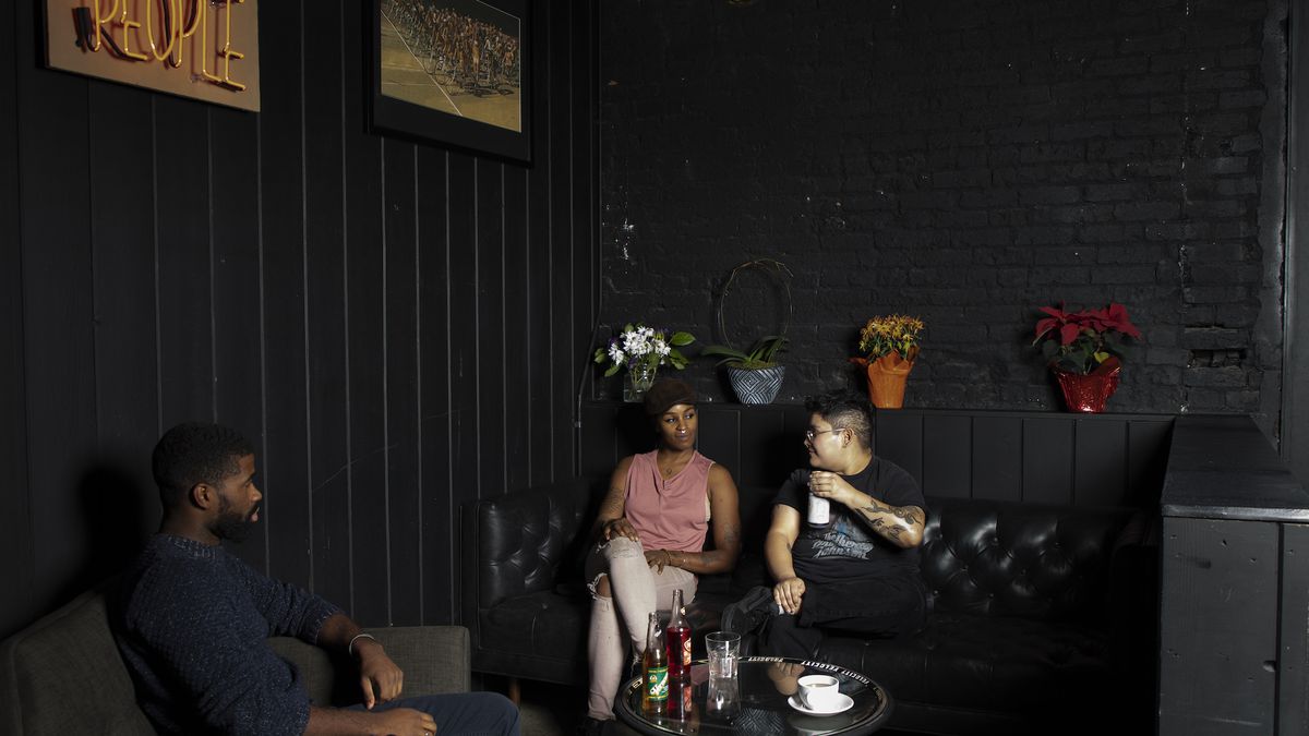 Three people sit and converse over non-alcoholic drinks inside of a dark lounge space.