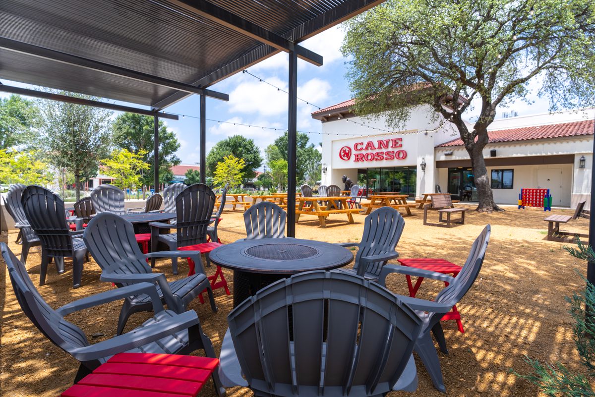 In the foreground, patio furniture at the patio of Cane Rosso in Hillcrest Village. Then, uncovered picnic tables. In the background, the restaurant’s facade. 