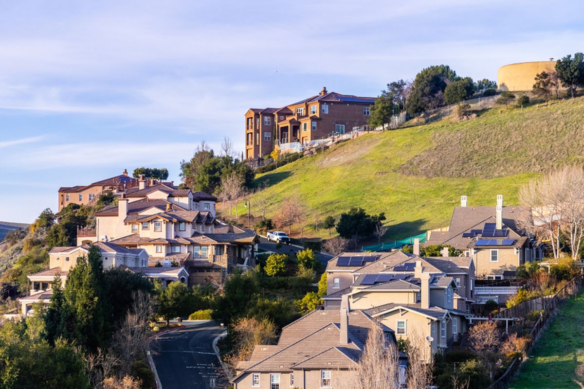 Residential neighborhood with multilevel single family homes, built on a hilly area; water tank visible on top of the hill.