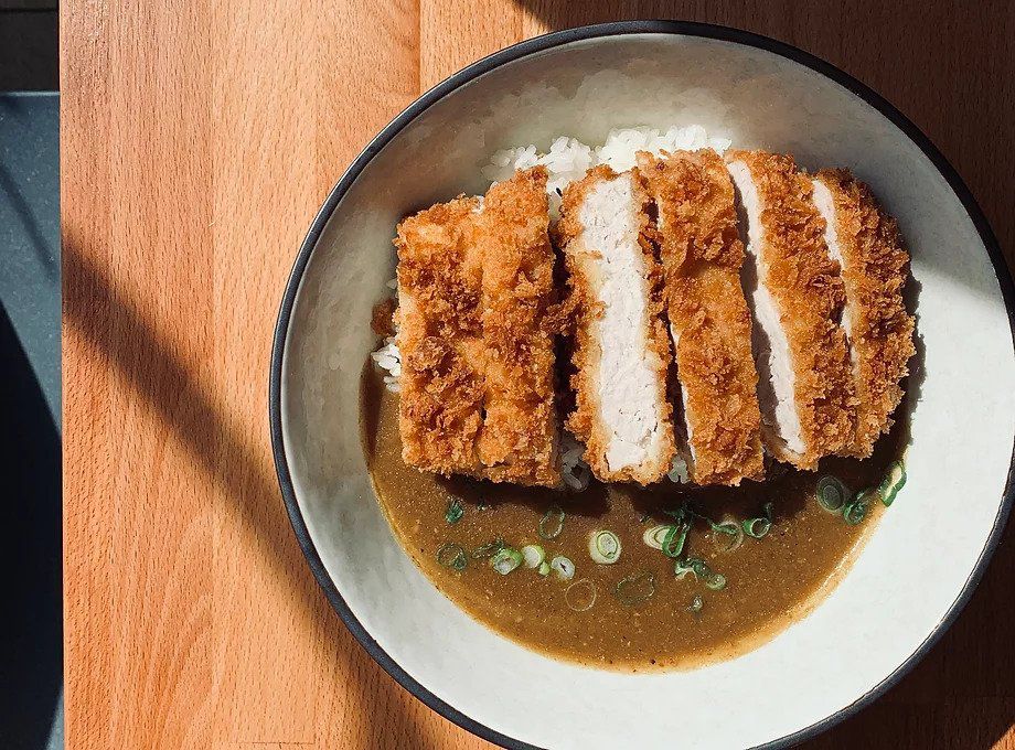 Thick slices of breaded chicken in a pool of curry on a white plate