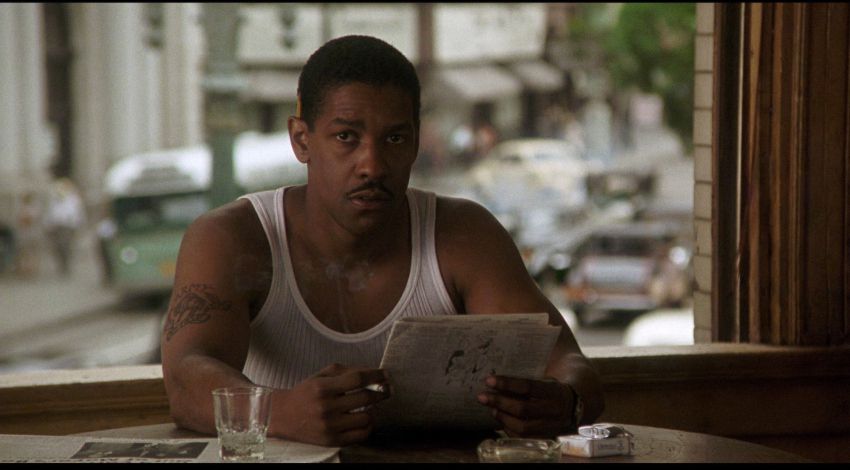 Denzel Washington, wearing a white tanktop, reads the newspaper in Devil in a Blue Dress.