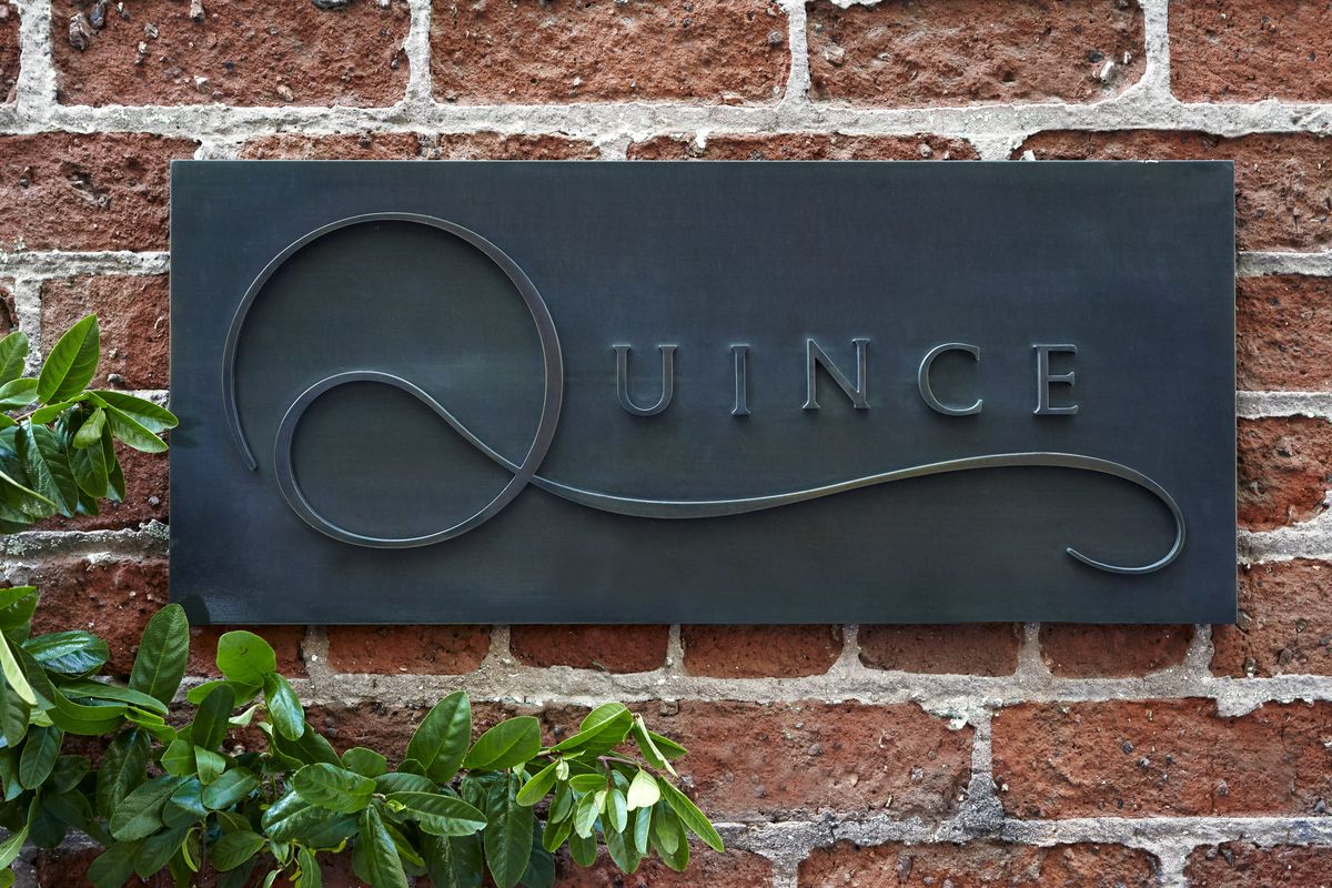 A sign on a brick wall that says “Quince.”