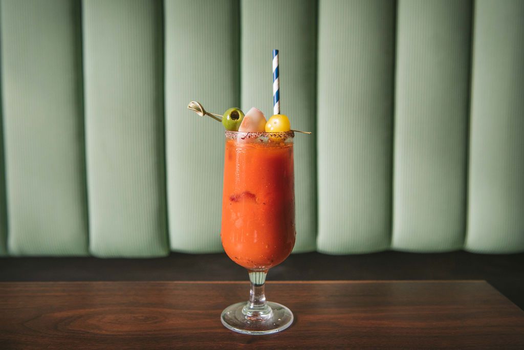 A bloody mary drink, with an olive topping and straw, sits on a table