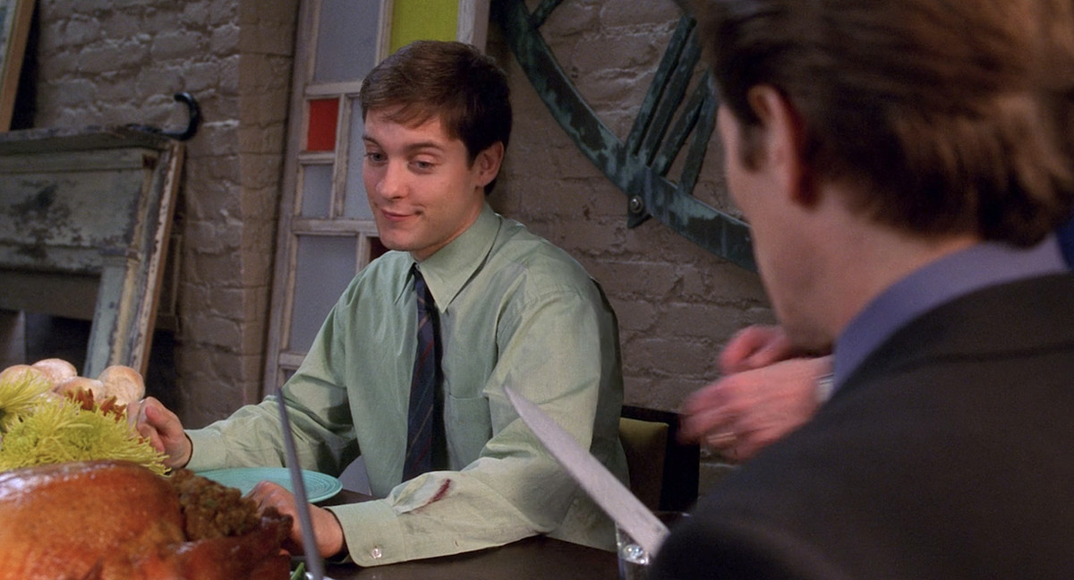 Peter Parker (Tobey Maguire) smiles sidelong at Norman Osborn (Willem Dafoe) as Norman starts to carve the turkey at Thanksgiving dinner in Sam Raimi’s 2002 Spider-Man