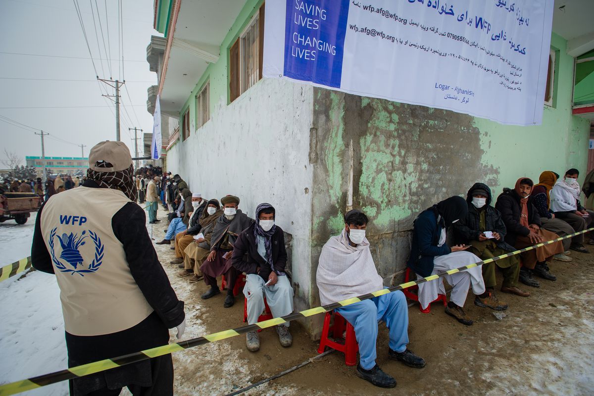 Afghans sit in a line stretching around the corner of a building as they wait for food to be distributed by the UN World Food Program (WFP) in Pul-e Alam, Afghanistan, on January 17, 2022.