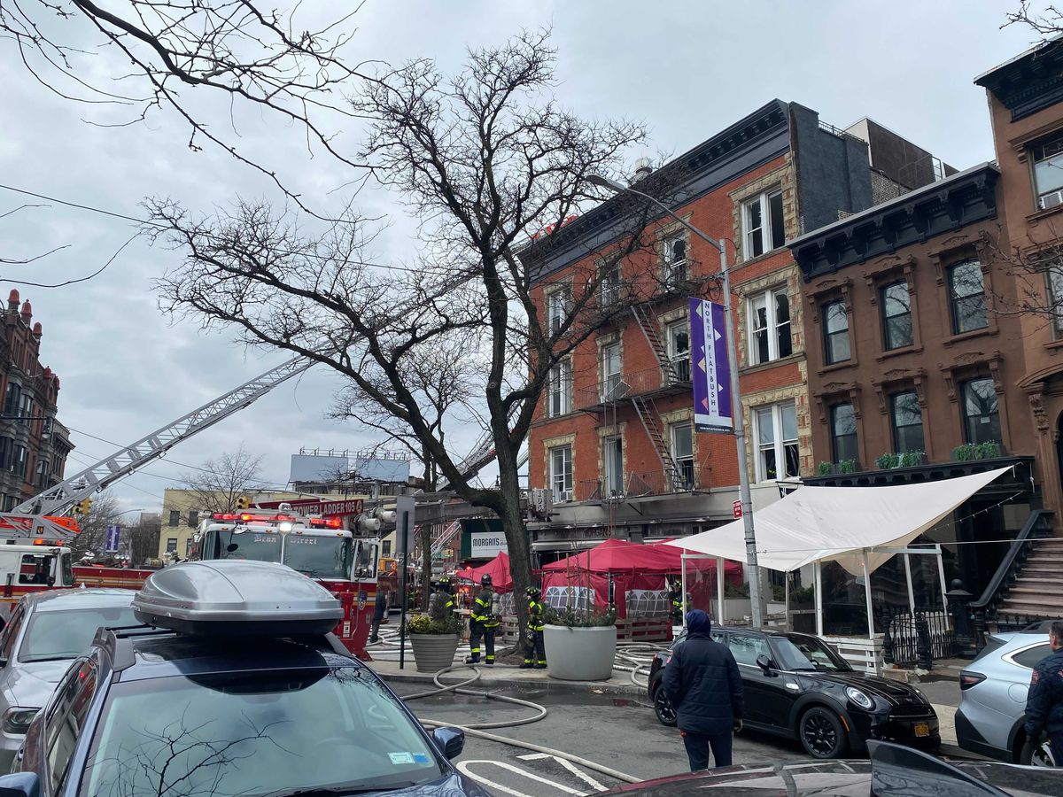 Several fire trucks are parked in front of a restaurant in New York City, with ladders propped against the top of the building