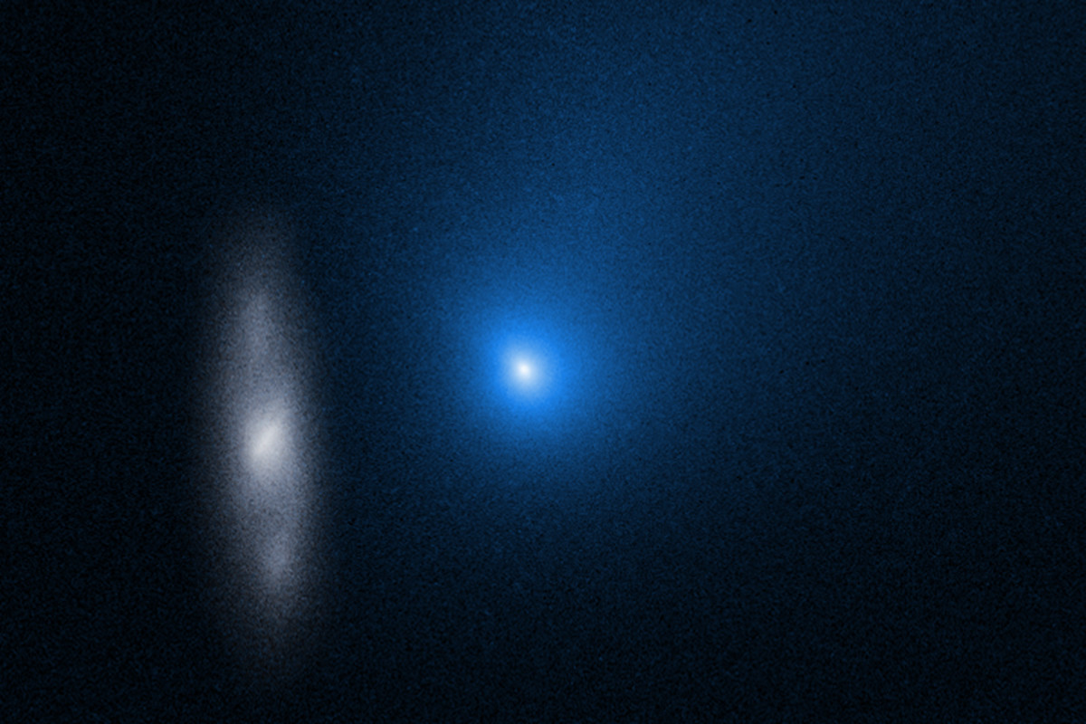 The comet appears as a glowing blue dot in this hubble space telescope image. To the left of it, is a spiral galaxy.