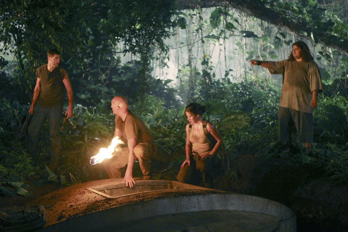 (L-R) Matthew Fox, Terry O’Quinn, Evangeline Lilly, and Jorge Garcia standing in front of a concrete hatch surrounded by a tropical forest in Lost.