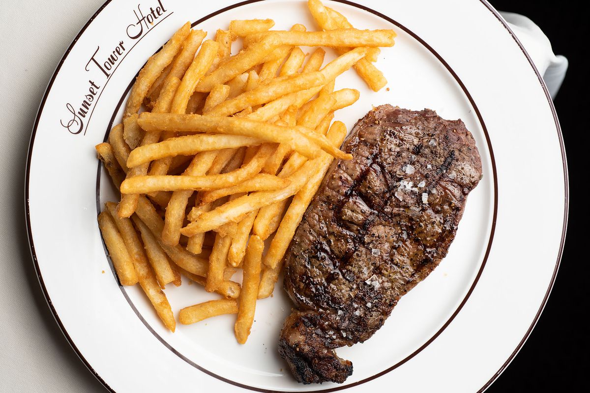 An overhead shot of a white plate with a cooked steak and pile of fries at Sunset Tower Bar in Los Angeles.