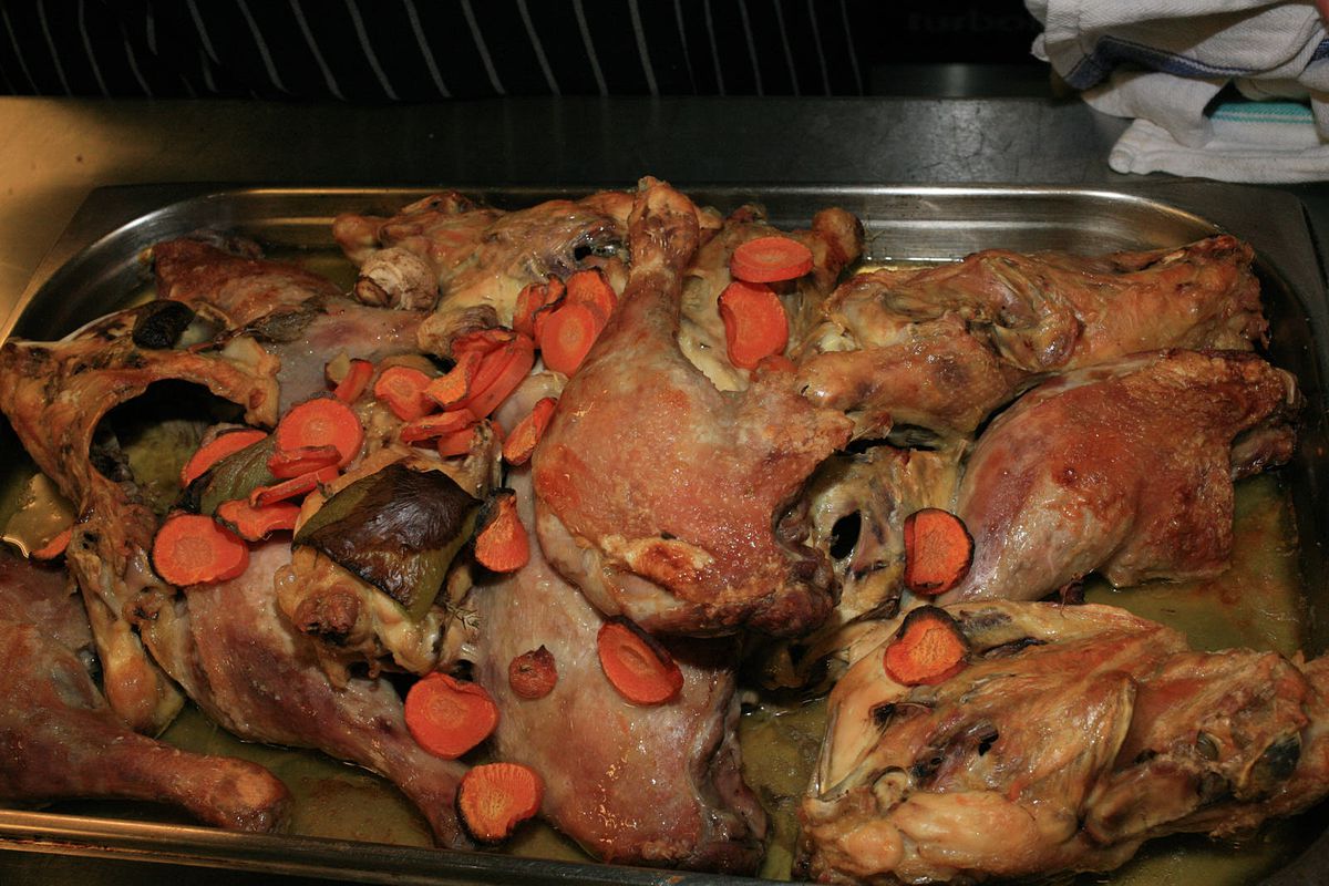 A closeup of a tray of roasted duck legs, carrots, mushrooms, celery, immersed in almost confit duck fat.