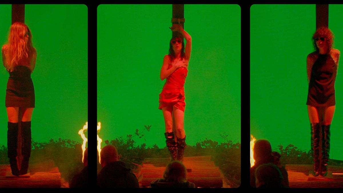 Three women in stylish dresses tied to stakes, lit in red, against a bright green background