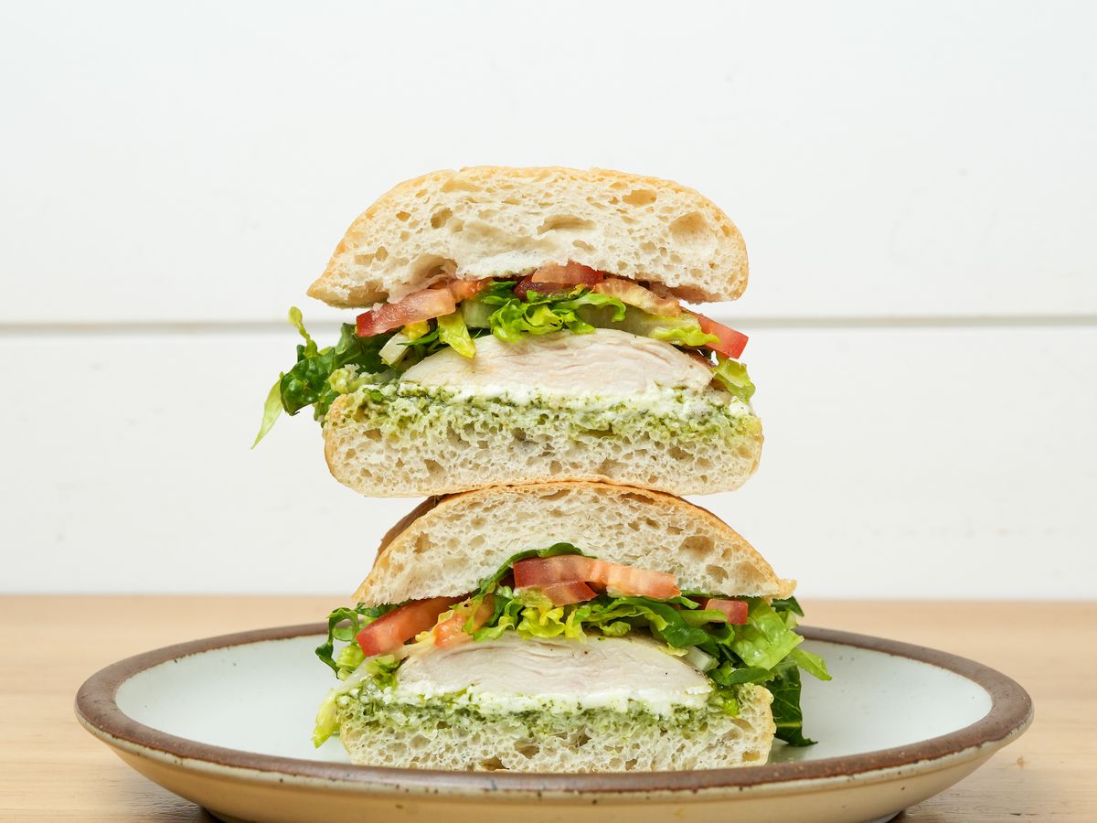 Two sides of a chicken pesto sandwich, topped with tomato and lettuce.