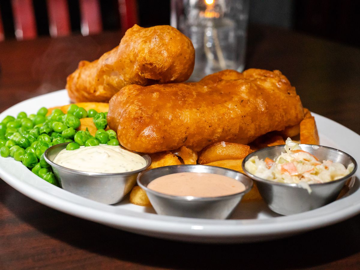A plate of fried, battered fish with peas and sauces.