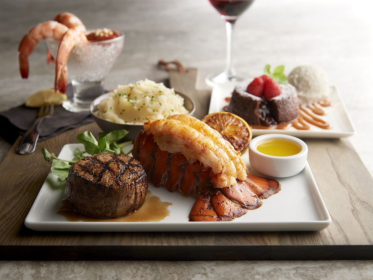 A white plate holds a steak and lobster.