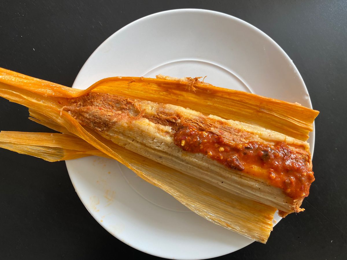 Pork tamal on a plate. topped with red salsa