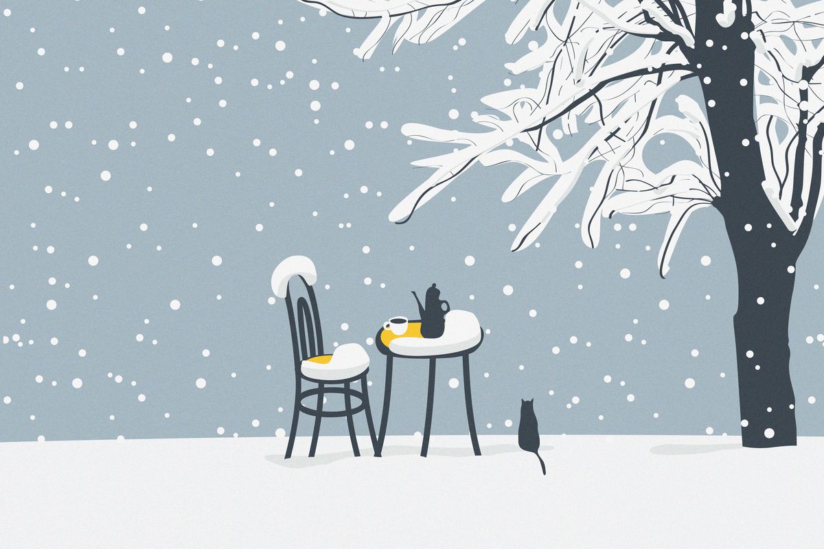 A chair and table are coated by falling snow. A cat sits next to the table. A tree, who’s branches are covered in snow, is in the background.