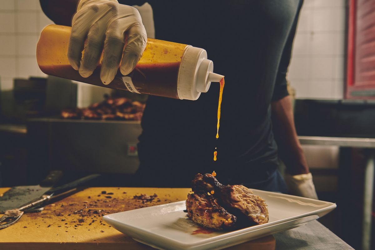 A hand pours sauce from a squeeze bottle onto a plate of jerk chicken.