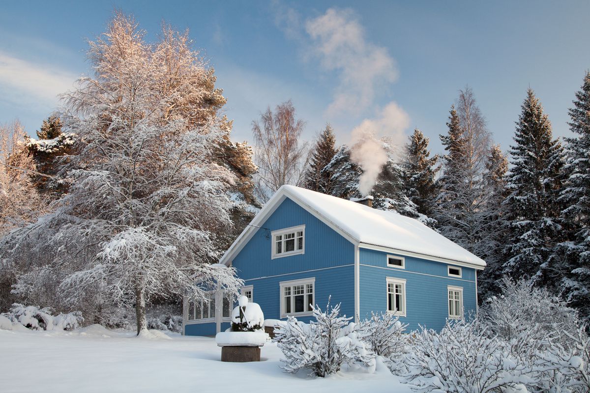 A snow covered blue house with smoke coming from the chimney