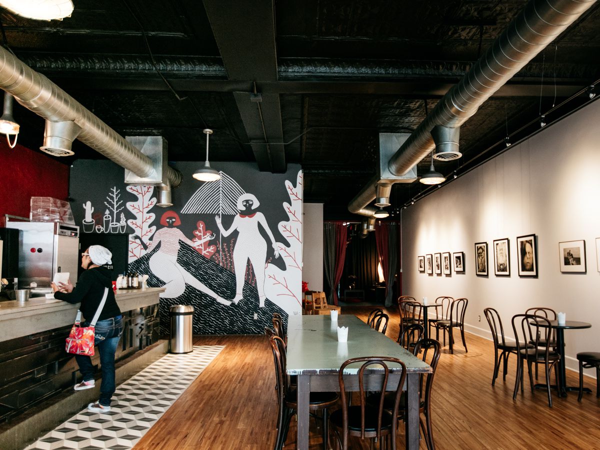 A coffee shop with a black and white interior and a mural with abstract mural of women in various poses.