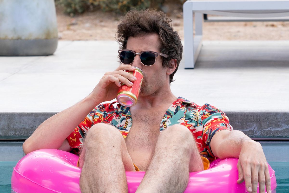 A man wearing sunglasses and a Hawaiian shirt floats in a pool drinking beer.