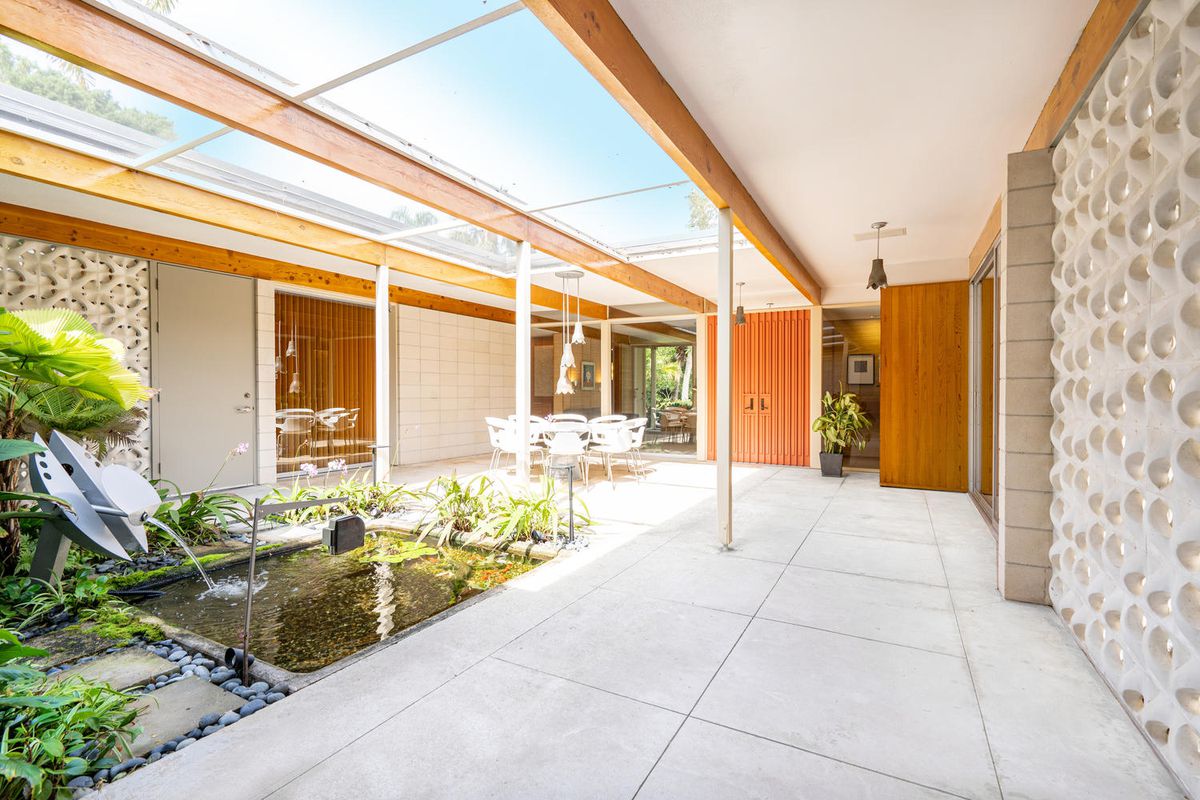 An interior covered courtyard features a pond, round dining set, and exposed beams.