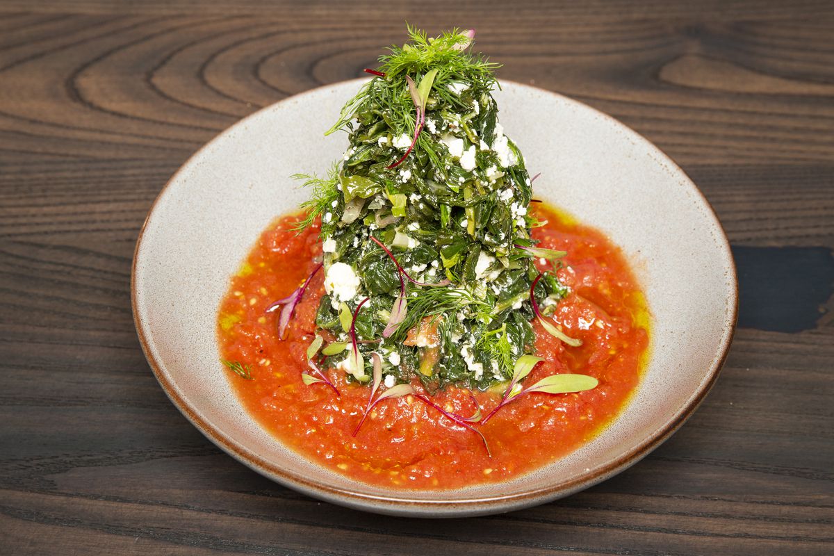 A round white bowl holds a light tomato sauce and a pile of braised greens mixed with feta.