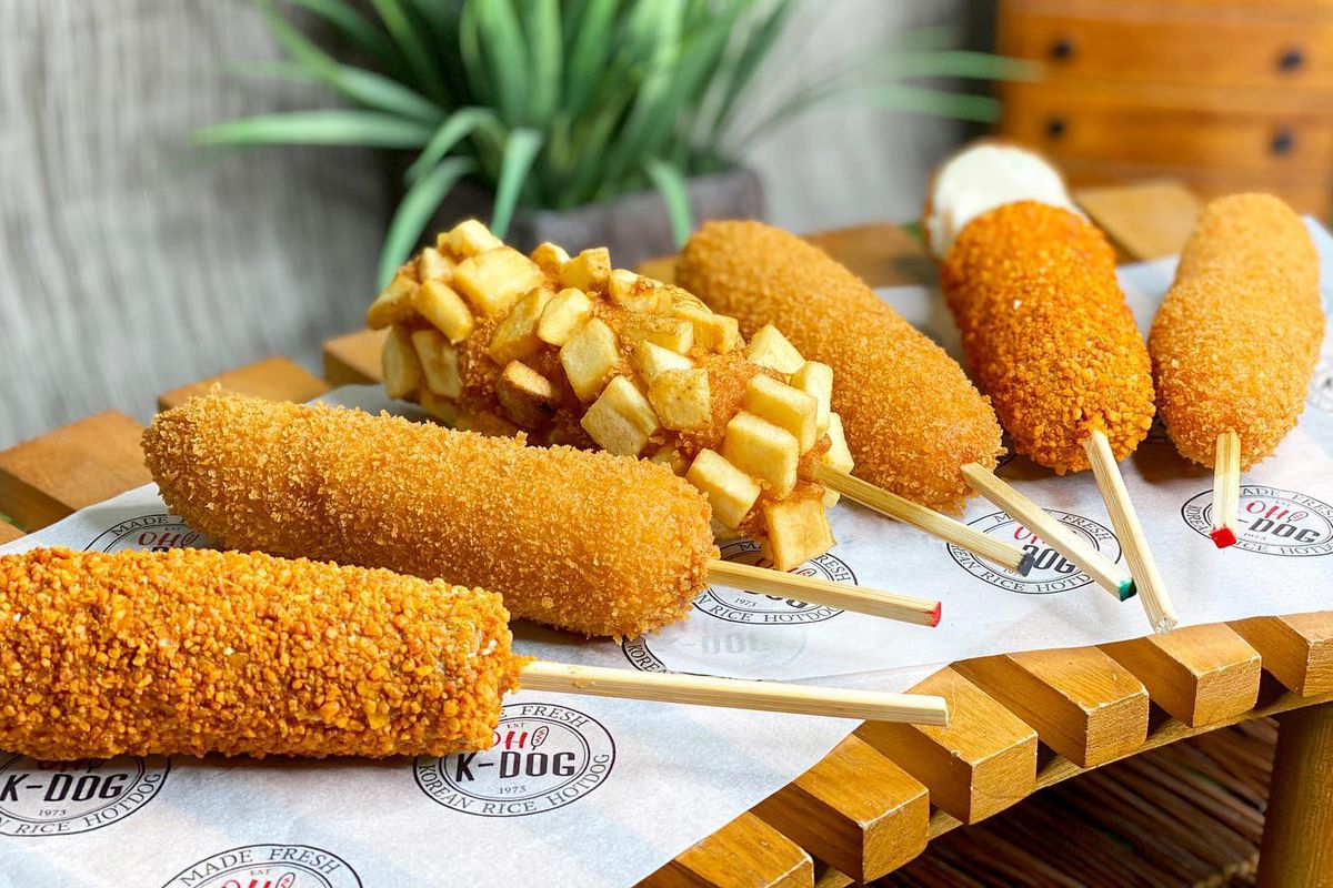 An array of crispy, panko-crusted corn dogs sitting on white paper atop a wooden board