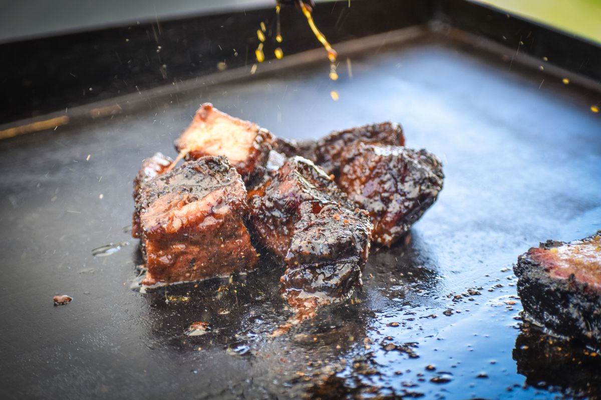 Sauce drizzling over a flat-top griddle filled with chunks of fatty pork belly at a pop-up restaurant.