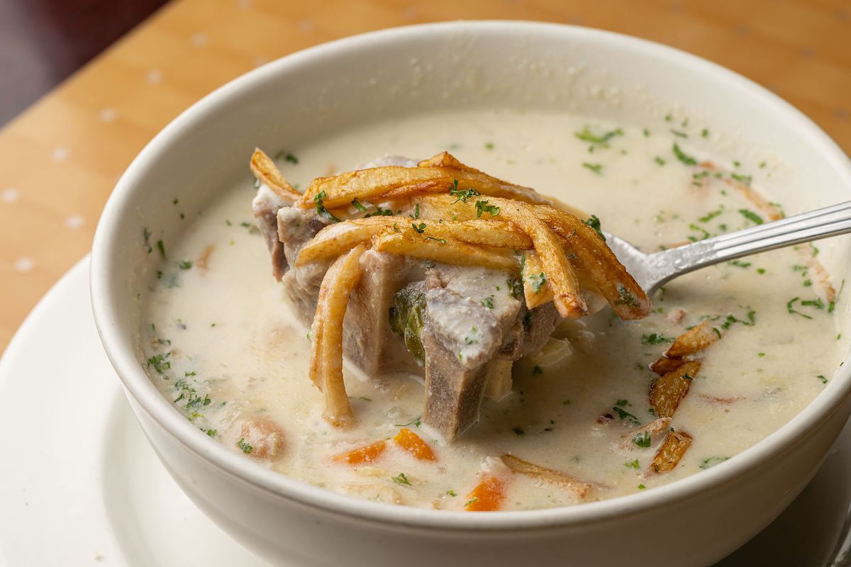 A spoon pulls up fries and beef from a white broth soup.