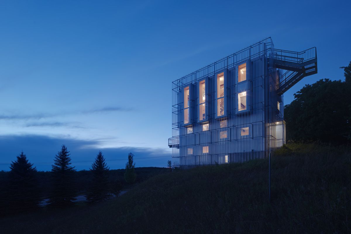 Steel tower clad in translucent plastic panels rises on hill at night. 