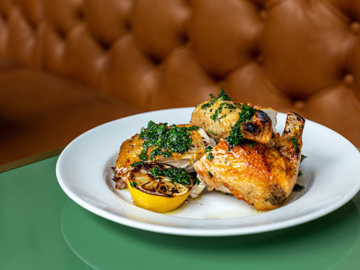 A plate of roasted chicken topped with salsa verde with a charred lemon on a green table.