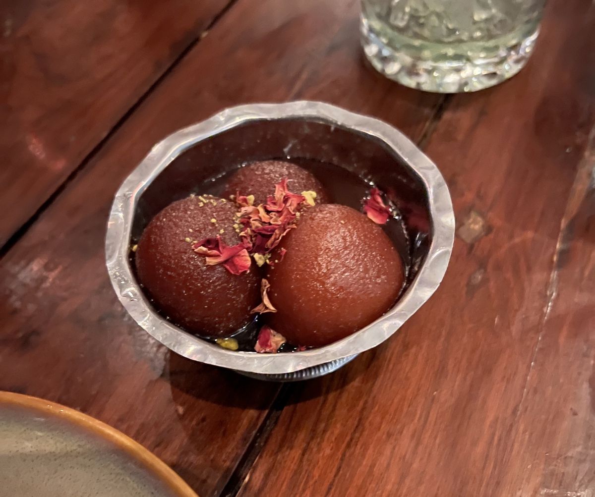 Three balls of fried dough float in syrup in a metal tin on a wooden table.