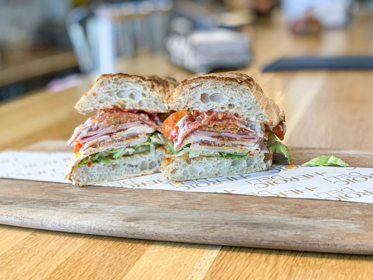 A stacked Italian sandwich from a new deli, on a wooden board.