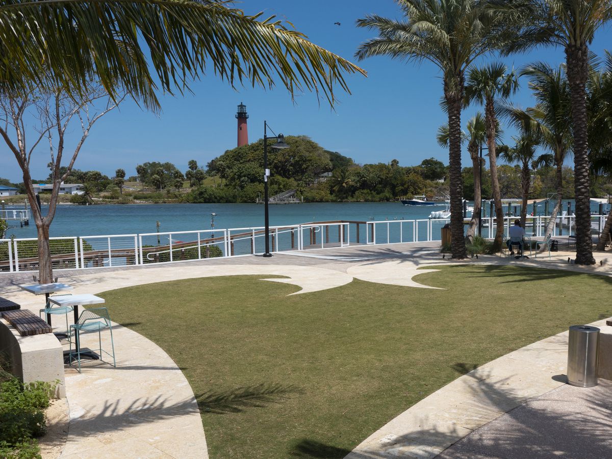 This picture is a view of the Jupiter Lighthouse as seen from Beacon restaurant. It’s across the Jupiter Inlet from the lighthouse. The sidewalk in the foreground is in the shape of a heart. There are also palm trees.