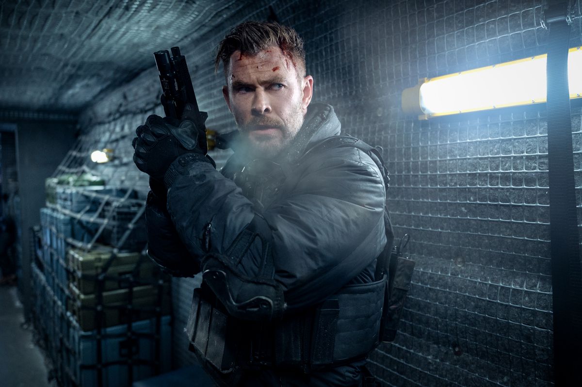 Chris Hemsworth as Tyler Rake holding a pistol, dressed in winter gear with flecks of blood visible on their forehead in Extraction 2.