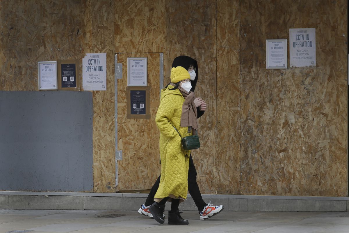 People walk past a boarded up nightclub near Leicester Square in central London, Thursday, Feb. 11, 2021. People are advised to stay at home to stay safe due to the coronavirus pandemic. 