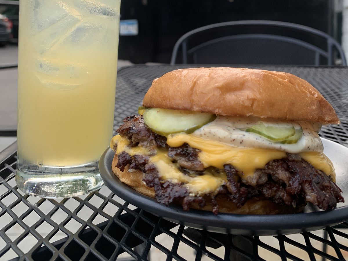 A cheeseburger and a cocktail on a table. 