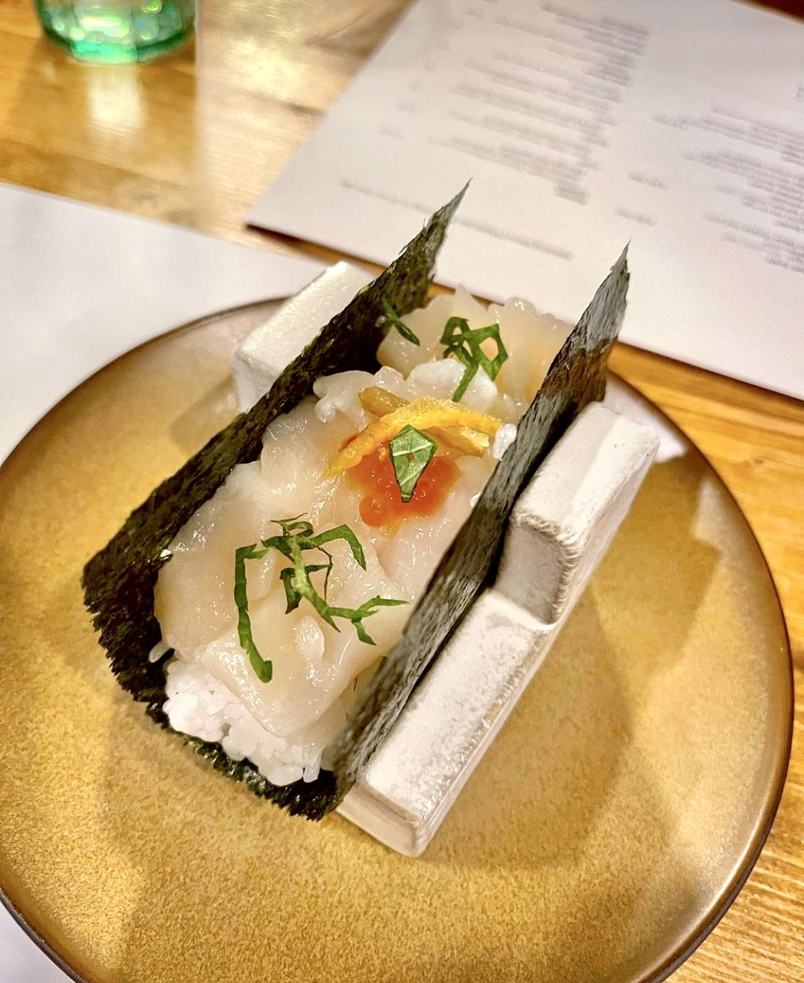 Raw scallops sit on a bed of sushi rice atop seaweed, which is folded in a taco-like shape.