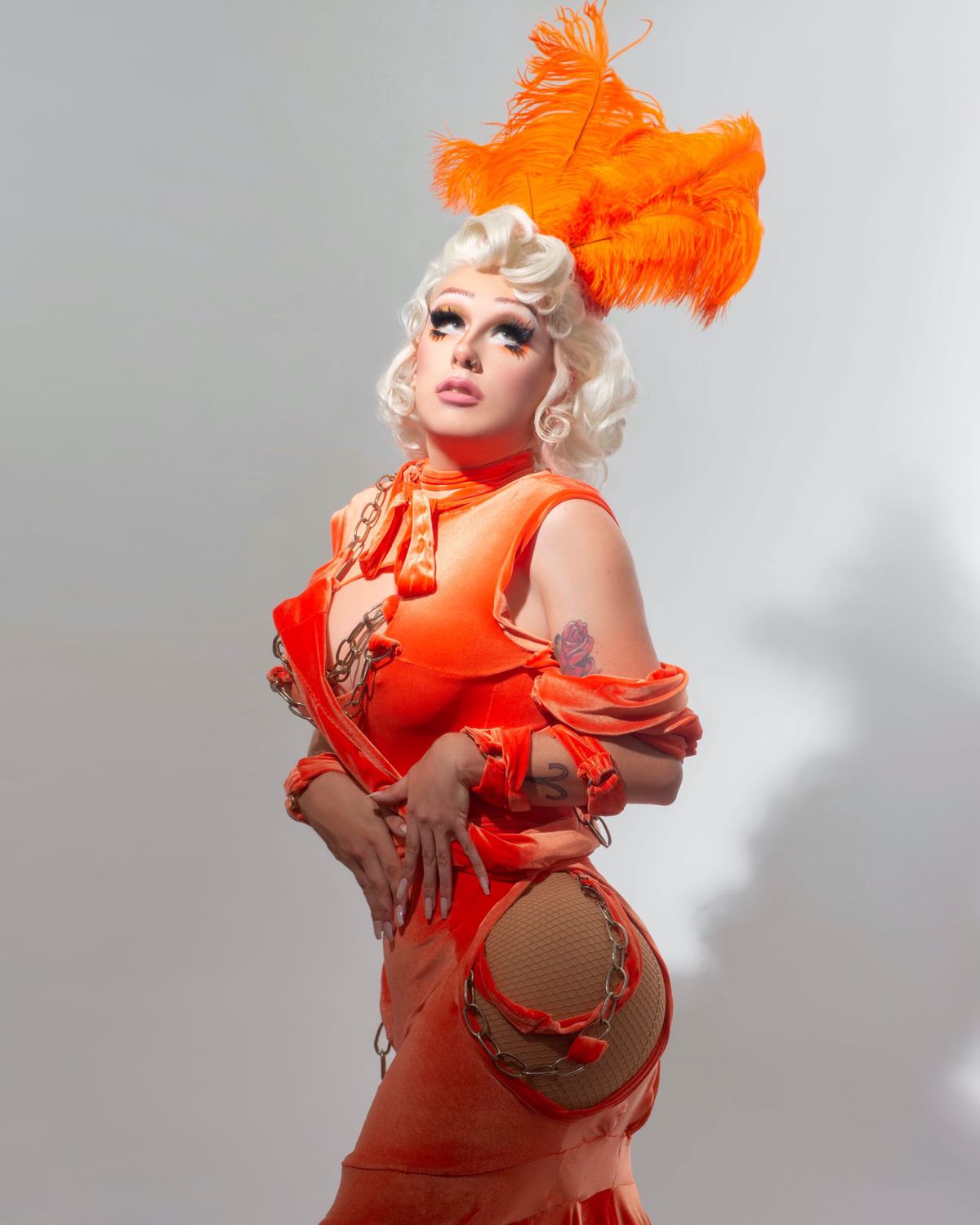 Drag queen Missy Steak is wearing a bright orange outfit, including a head feather.