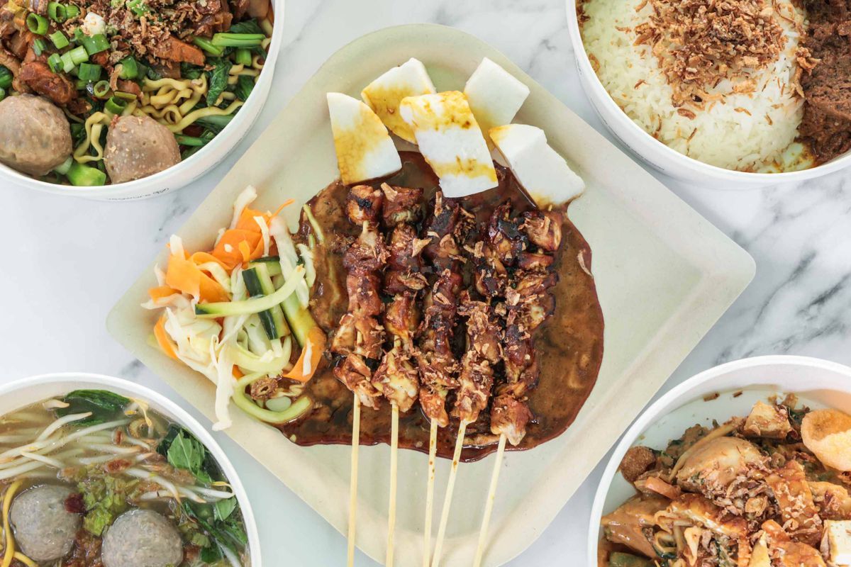 A birdseye view of satay chicken skewers, fish balls, and beef rendang with rice and crispy shallots.