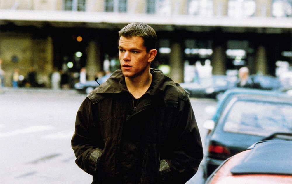 Matt Damon wearing a dark green jacket while walking down a street in The Bourne Identity.