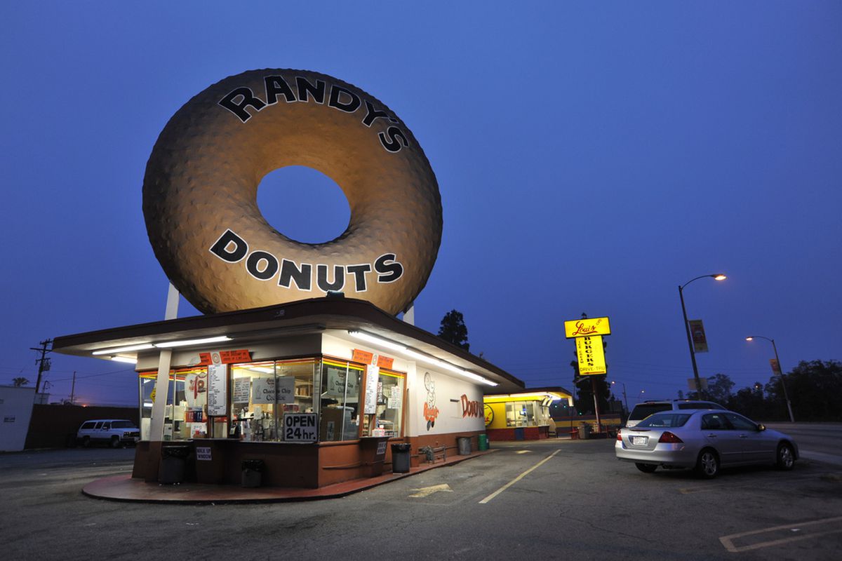 A building with a giant doughnut on the roof with a dark sky.