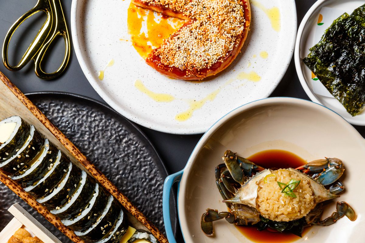 An assortment of dishes at Kawi, including raw blue crab, its shell stuffed with rice, and a pinwheel of roasted rice cake, which is dark red and topped with sesame seeds