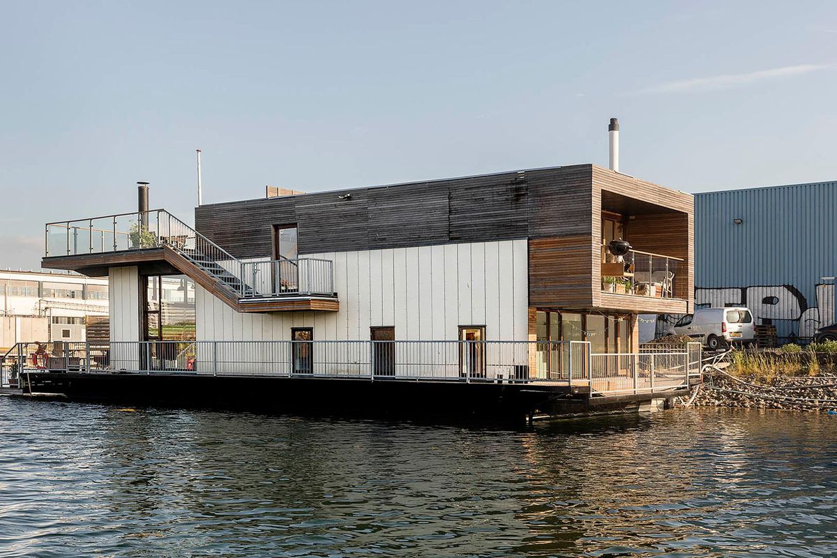 A cubic modern houseboat sits in Copenhagen’s Teglholmen harbor, and features plenty of outdoor terrace space in addition to its high-ceilinged living room and two bedrooms. Plenty of high-ceilinged windows allow for sweeping views of the harbor, and outd