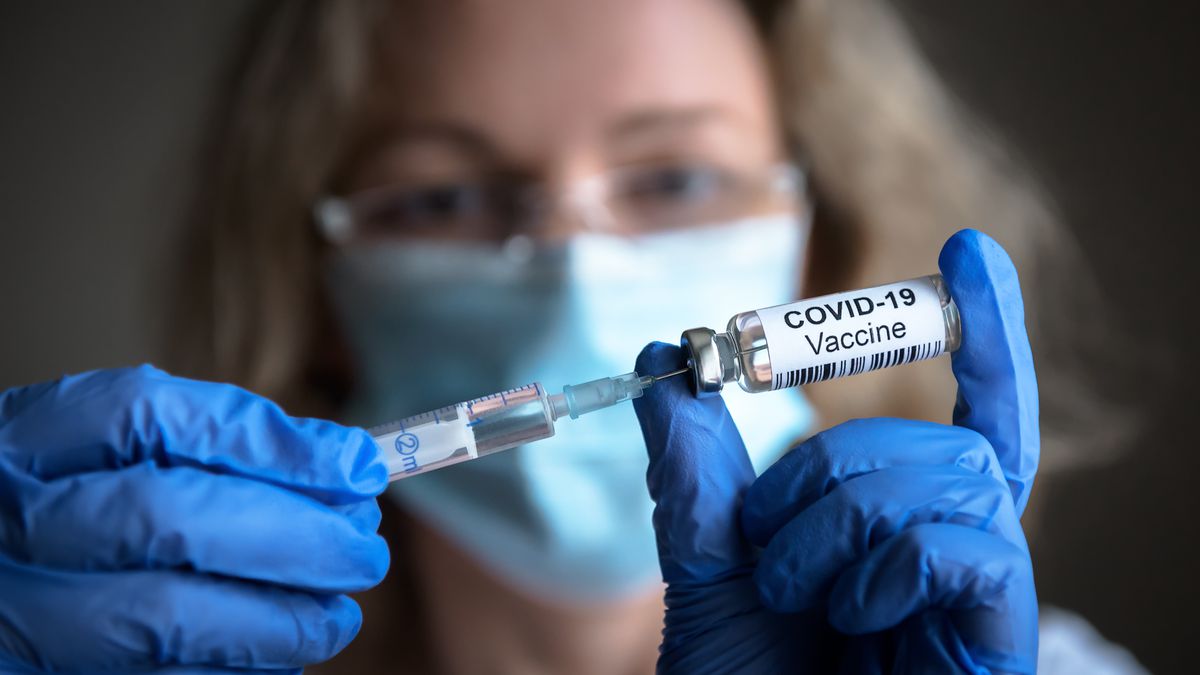 A woman with gloves, a mask, and goggles on fills up a syringe with the COVID-19 vaccine