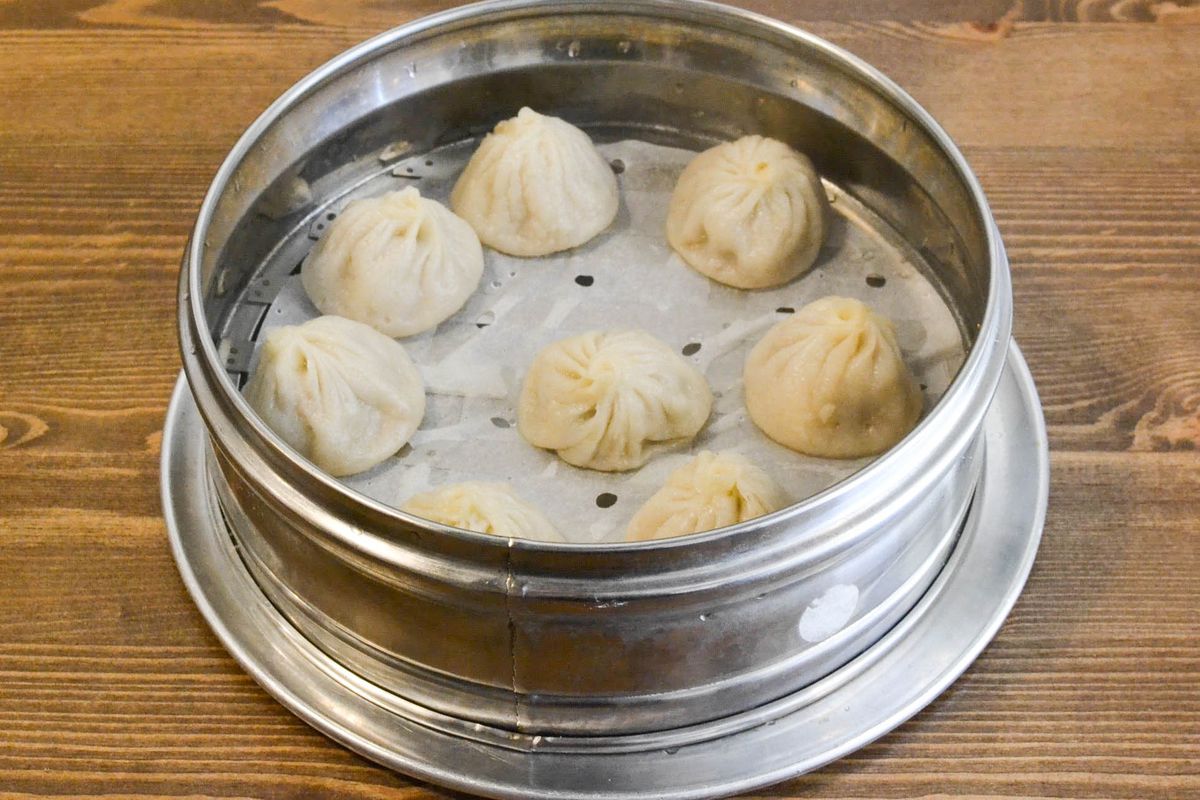 xiao long bao dumplings in a metal tin on a wooden table.