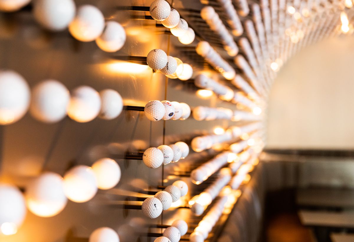 A curved wall studded with golf balls and hanging lights
